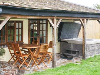 An outdoor covered patio with wooden table and chairs and a hot tub at Brambles Cottage in Little Malvern near Malvern