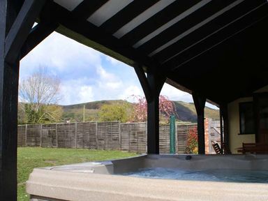 A covered patio with a hot tub and wooden fence with hills in the background at Brambles Cottage in Little Malvern near Malvern
