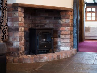 A brick fireplace with a black stove inside and a tiled floor at Brambles Cottage in Little Malvern near Malvern