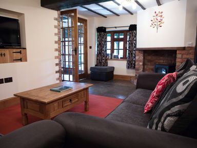 A living room with a gray sofa and patterned cushions a wooden coffee table a fireplace and a TV at Brambles Cottage in Little Malvern near Malvern