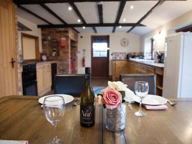 A dining table set with wine glasses plates a bottle of wine and flowers in a kitchen at Brambles Cottage in Little Malvern near Malvern