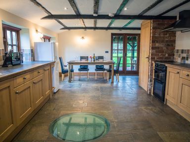 A kitchen with wooden cabinets a dining table with chairs a refrigerator and glass doors at Brambles Cottage in Little Malvern near Malvern