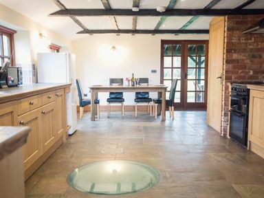 A kitchen with wooden cabinets dining table with chairs and glass floor panel at Brambles Cottage in Little Malvern near Malvern