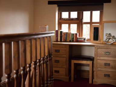 A wooden desk with drawers and books next to a window with a stool underneath at Brambles Cottage in Little Malvern near Malvern