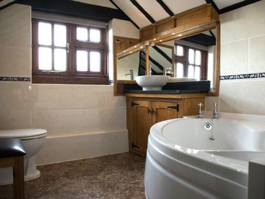 A bathroom with a bathtub toilet wooden vanity and window at Brambles Cottage in Little Malvern near Malvern
