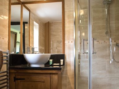 A bathroom with a round sink on a black countertop wooden cabinet a mirror and a glass shower enclosure at Brambles Cottage in Little Malvern near Malvern