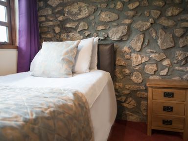 A bedroom with a bed next to a stone wall and a wooden nightstand at Brambles Cottage in Little Malvern near Malvern