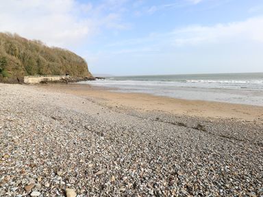 A beach with pebbles and sand near a wooded cliff by the sea at The Garden Flat in Saundersfoot