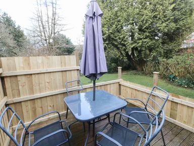 An outdoor patio with a glass table and four metal chairs around it and a closed umbrella in the center at The Garden Flat in Saundersfoot