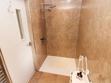 A walk-in shower with brown tiled walls a white shower tray and a small white stand holding toiletries at The Garden Flat in Saundersfoot
