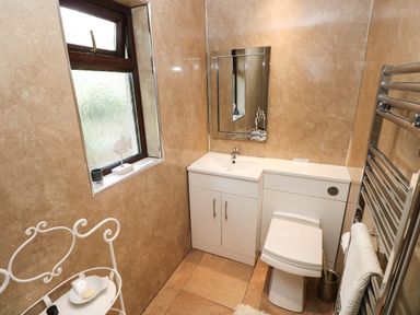 A bathroom with a white sink cabinet and toilet beside a frosted window and a metal towel rack with a towel at The Garden Flat in Saundersfoot