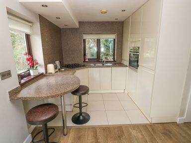 A kitchen with a breakfast bar, two stools, countertop appliances, a sink, an oven, and a window at The Garden Flat in Saundersfoot