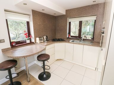A kitchen with a countertop stove sink toaster kettle two stools and two windows at The Garden Flat in Saundersfoot