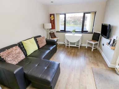 A living room with a black leather sofa and cushions a small folding table with a vase near a window and two white chairs at The Garden Flat in Saundersfoot