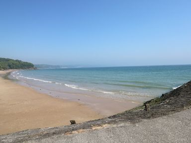 A sandy beach with gentle waves and a clear sky with trees on the left at The Garden Flat in Saundersfoot