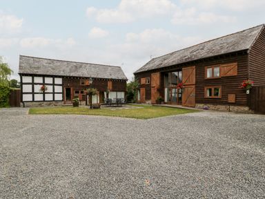 Two barn style buildings with wooden cladding and stone foundations a gravel courtyard and a lawn area with outdoor furniture at Stable End in Luntley near Pembridge