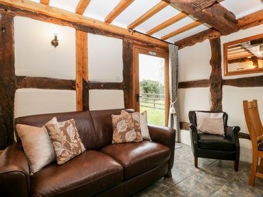 A sitting area with a brown leather sofa and armchair near a door with exposed wooden beams on walls and ceiling at Stable End in Luntley near Pembridge