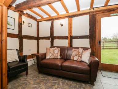 A sitting area with a brown leather sofa, black armchair, side table, wall lights, and a door opening to a garden at Stable End in Luntley near Pembridge