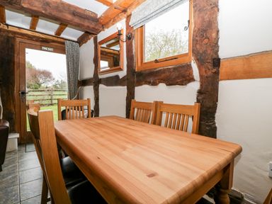 A dining area with a wooden table and chairs next to a window and door with exposed wooden beams at Stable End in Luntley near Pembridge
