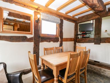 A dining area with wooden table and chairs in a room with exposed wooden beams and a wall-mounted TV at Stable End in Luntley near Pembridge