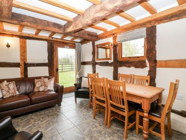 A dining area with wooden table and chairs and a leather sofa in a room with exposed wooden beams at Stable End in Luntley near Pembridge