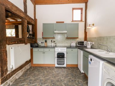 A kitchen with green cabinets white appliances and exposed wooden beams at Stable End in Luntley near Pembridge