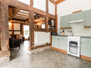 A kitchen area with green cabinets and a white stove next to a wooden framed living space with chairs at Stable End in Luntley near Pembridge