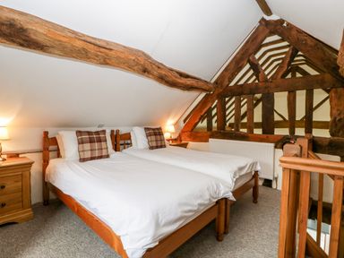 A bedroom with two single beds, wooden beams, bedside tables with lamps, and a wooden railing at Stable End in Luntley near Pembridge