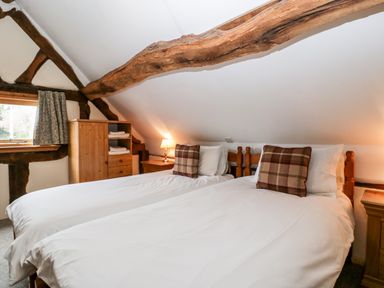 A bedroom with two single beds with checkered pillows wooden furniture and exposed wooden beams at Stable End in Luntley near Pembridge