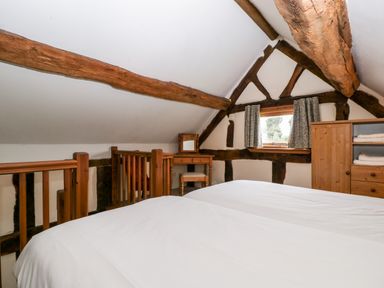 A bedroom with wooden beams a small window a desk with a mirror and a wooden wardrobe at Stable End in Luntley near Pembridge