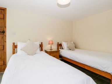 A bedroom with two single beds and a wooden nightstand with a lamp at Stable End in Luntley near Pembridge