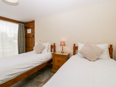 A bedroom with two single beds a wooden nightstand and a lamp at Stable End in Luntley near Pembridge