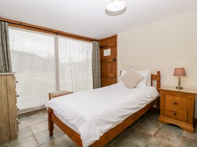 A bedroom with a single bed white bedding wooden furniture and a window with curtains at Stable End in Luntley near Pembridge