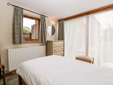 A bedroom with a bed a wooden dresser a chair and windows with curtains at Stable End in Luntley near Pembridge