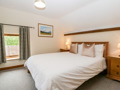 A bedroom with a bed with white bedding two bedside tables with lamps and a window with curtains at Stable End in Luntley near Pembridge