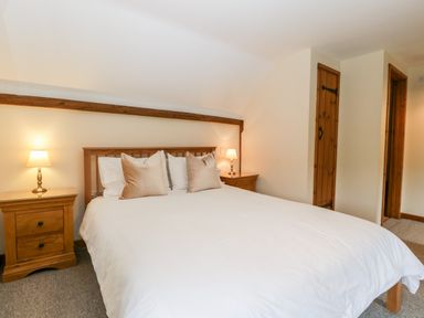 A bedroom with a bed with white bedding and beige pillows wooden bedside tables with lamps at Stable End in Luntley near Pembridge