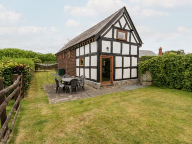 A small black and white timber framed building with a patio table and chairs on a paved area and green grass surrounding it at Stable End in Luntley near Pembridge