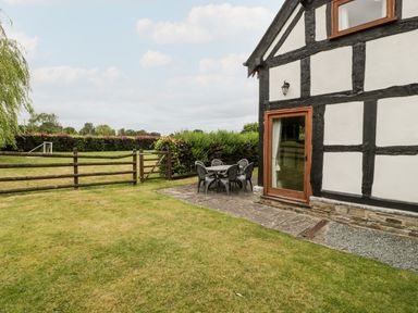 A garden area with a wooden fence and outdoor table and chairs beside a white and black timber house at Stable End in Luntley near Pembridge