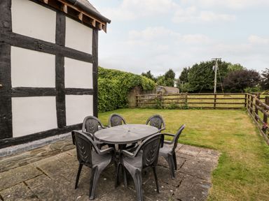 An outdoor patio with a black plastic table and six chairs next to a building with black and white timber framing at Stable End in Luntley near Pembridge