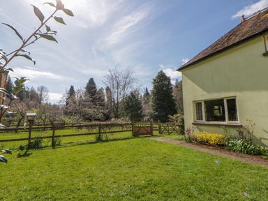 A garden with grass, a gate, and trees at Gardener's Cottage in Llanwrthwl near Rhayader
