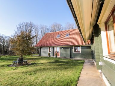 A green wooden house with a red tiled roof and a tree with a circular bench on a grass lawn at Apple Tree Lodge Swarland near Alnwick