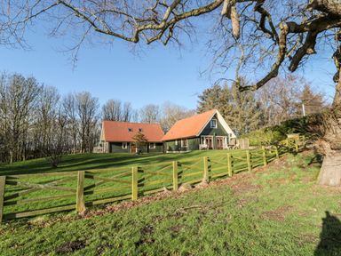 A wooden fence enclosing two houses with red roofs on a grassy hill surrounded by trees at Apple Tree Lodge in Swarland near Alnwick