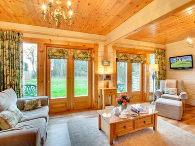 A living room with wooden ceiling and large windows showing greenery outside at Apple Tree Lodge Swarland near Alnwick