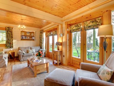 A living room with sofas coffee table lamp bookshelf and windows showing garden at Apple Tree Lodge Swarland near Alnwick