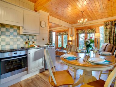 A kitchen and dining area with a wooden table set with plates and glasses a vase with flowers an oven and cupboards at Apple Tree Lodge Swarland near Alnwick