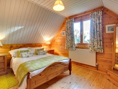 A bedroom with a wooden bed and green pillows and covers a wooden floor and two bedside tables with lamps at Apple Tree Lodge Swarland near Alnwick