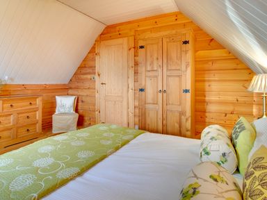 A bedroom with wooden walls a bed with pillows a chest of drawers a chair a wardrobe and a door at Apple Tree Lodge Swarland near Alnwick