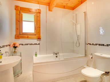 A bathroom with a bathtub shower toilet sink and a small glass shelf with flowers at Apple Tree Lodge Swarland near Alnwick