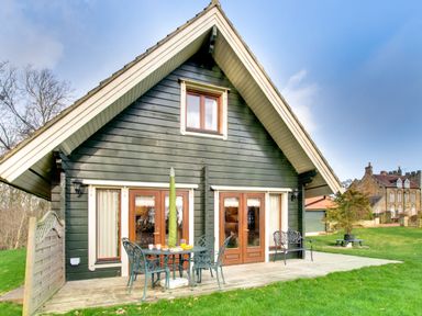 The exterior of a wooden cabin with patio furniture on a deck and a lawn at Apple Tree Lodge Swarland near Alnwick