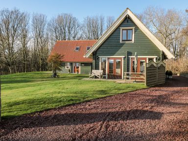 A house with green siding and a red roof on a grassy lawn with trees in the background at Lime Tree Lodge in Swarland near Alnwick